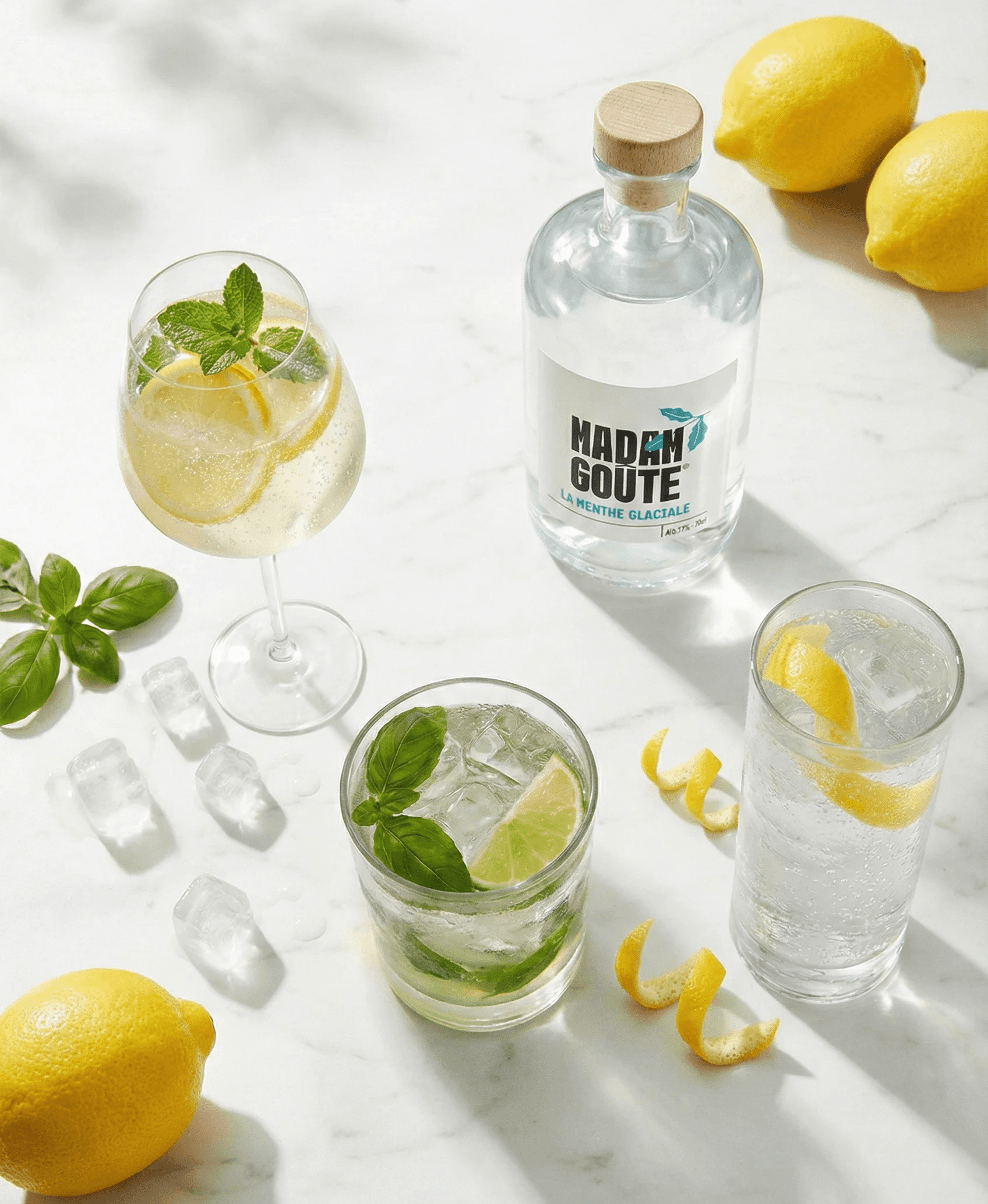 Liqueur Madame Goute Menthe Glaciale avec des cocktails rafraîchissants à la menthe et des agrumes frais sur un marbre brillant.