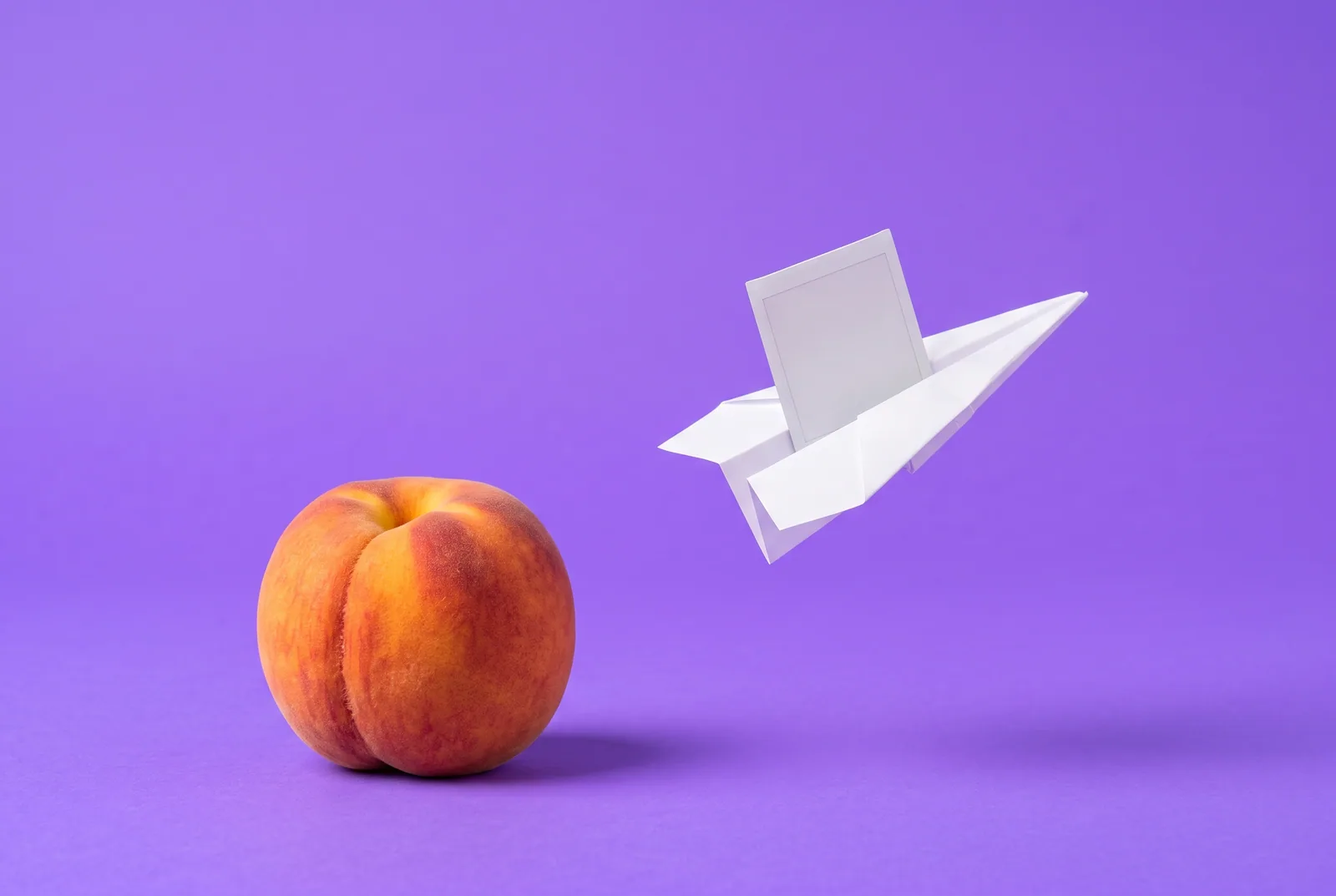 A paper airplane carrying a blank photo away from a peach, the risk of leaks in sexting addiction