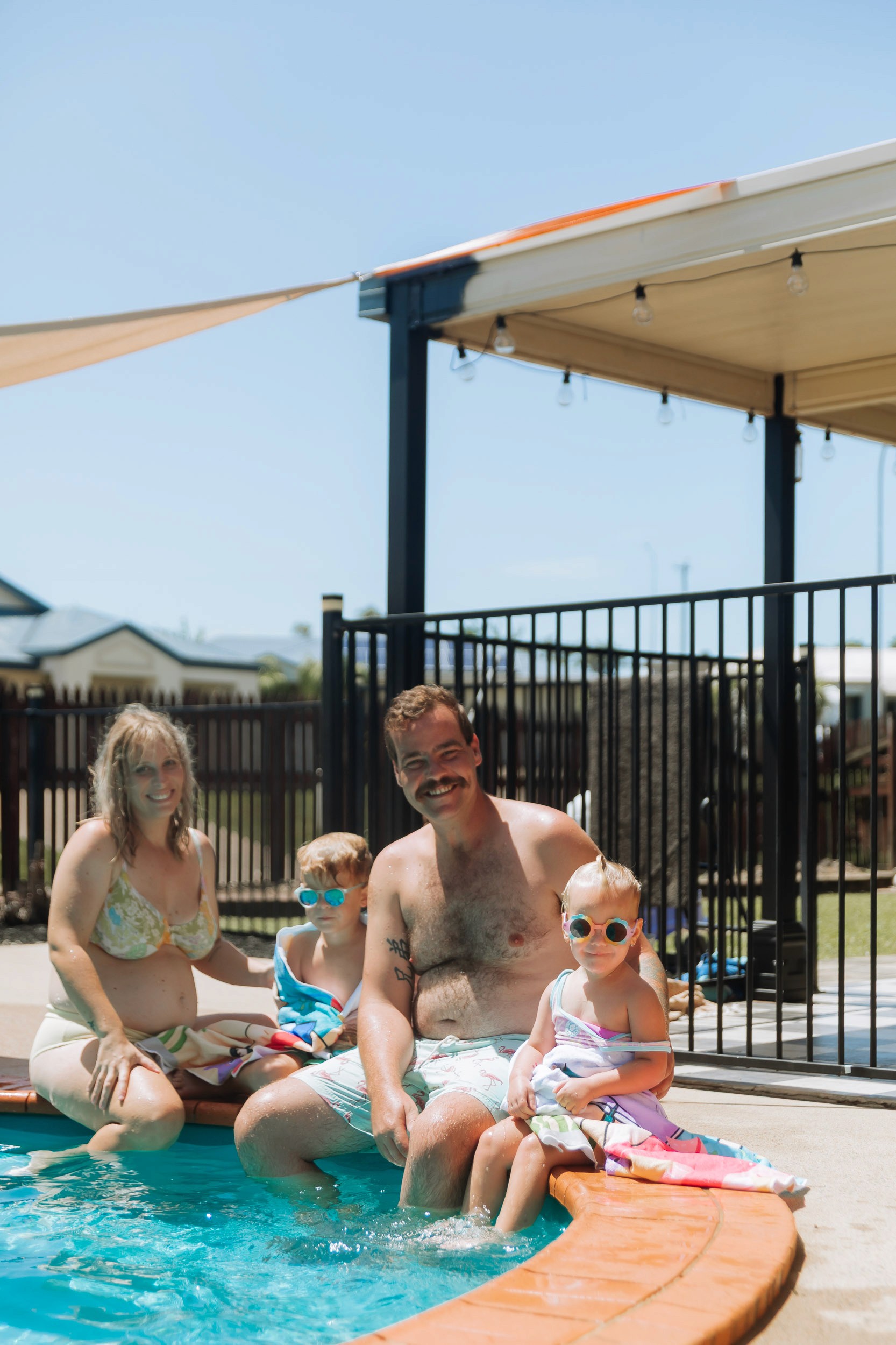 Relaxed lifestyle maternity session at home with a pregnant mother, dad and two young kids swimming together in the pool.