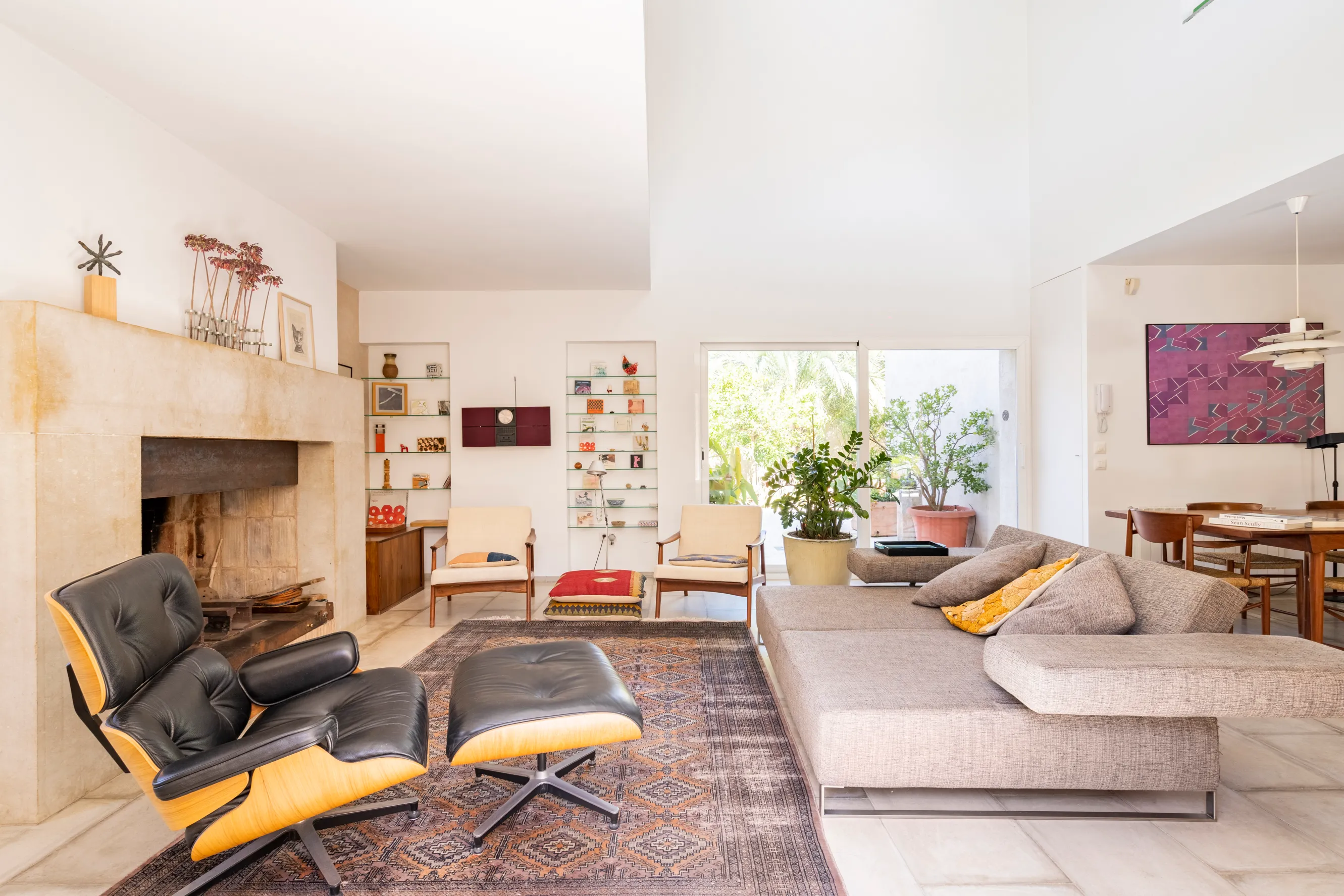 Bright and modern living room with a stone fireplace, mid-century furniture, and large sliding glass doors leading to outdoor greenery.