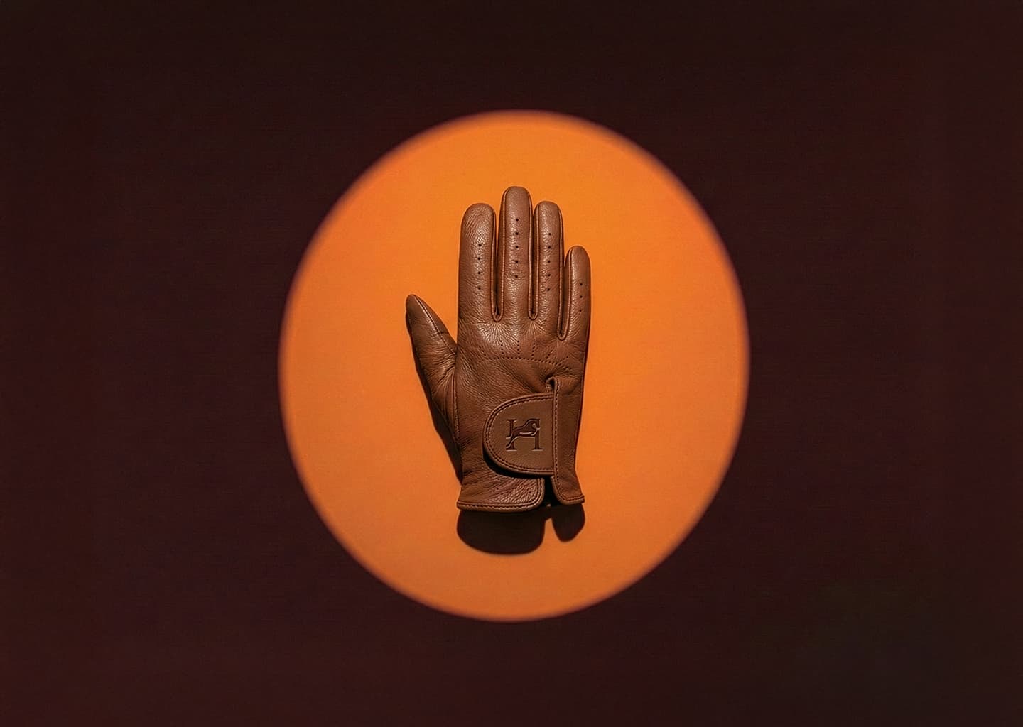 Gant en cuir marron de luxe Harlington, vue de face, avec logo embossé, photographié en studio sur fond circulaire orange.