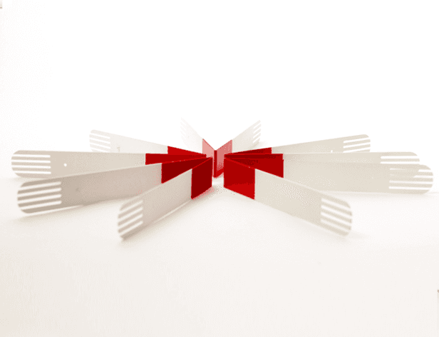A white, fan-shaped object with red bands is centered on a white background. The object is composed of multiple white plastic forks arranged symmetrically around a central red rectangular piece. The forks are evenly spaced and point outward from the central red piece. The object is flat and appears to be made of a lightweight material.