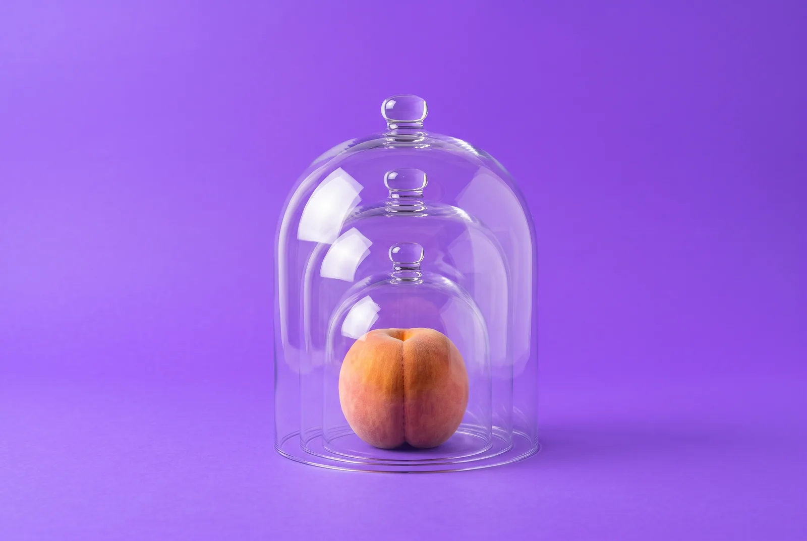 A ripe peach under three nested clear glass cloches on a violet backdrop, layered protection for how to block Pornhub on every device