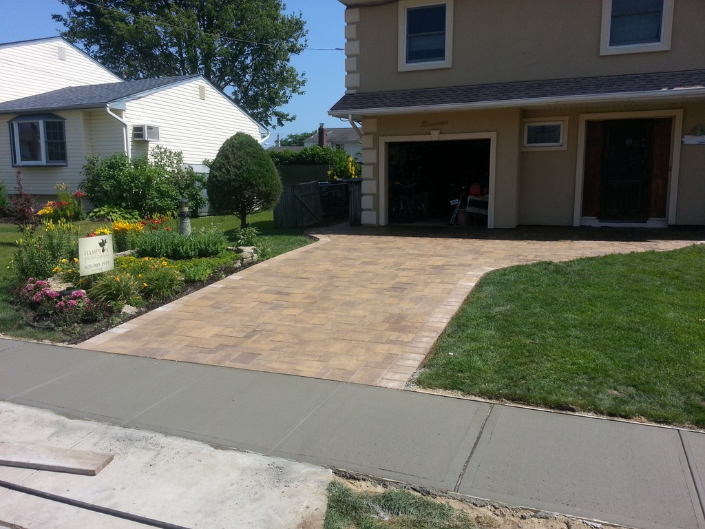 Tan paver driveway leading to single-car garage with garden landscaping