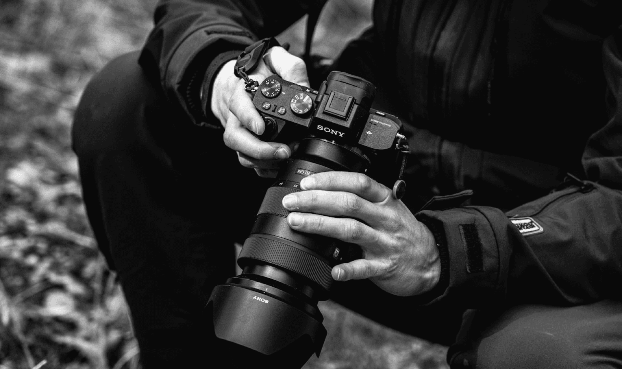 Black and white (Grayscale) picture of a man hodling a camera with lenses