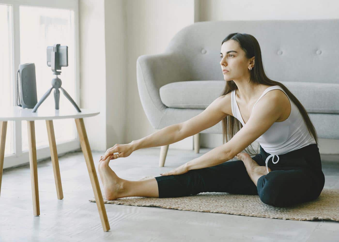 Woman in living room stretching on floor looking at phone on tripod in front of her
