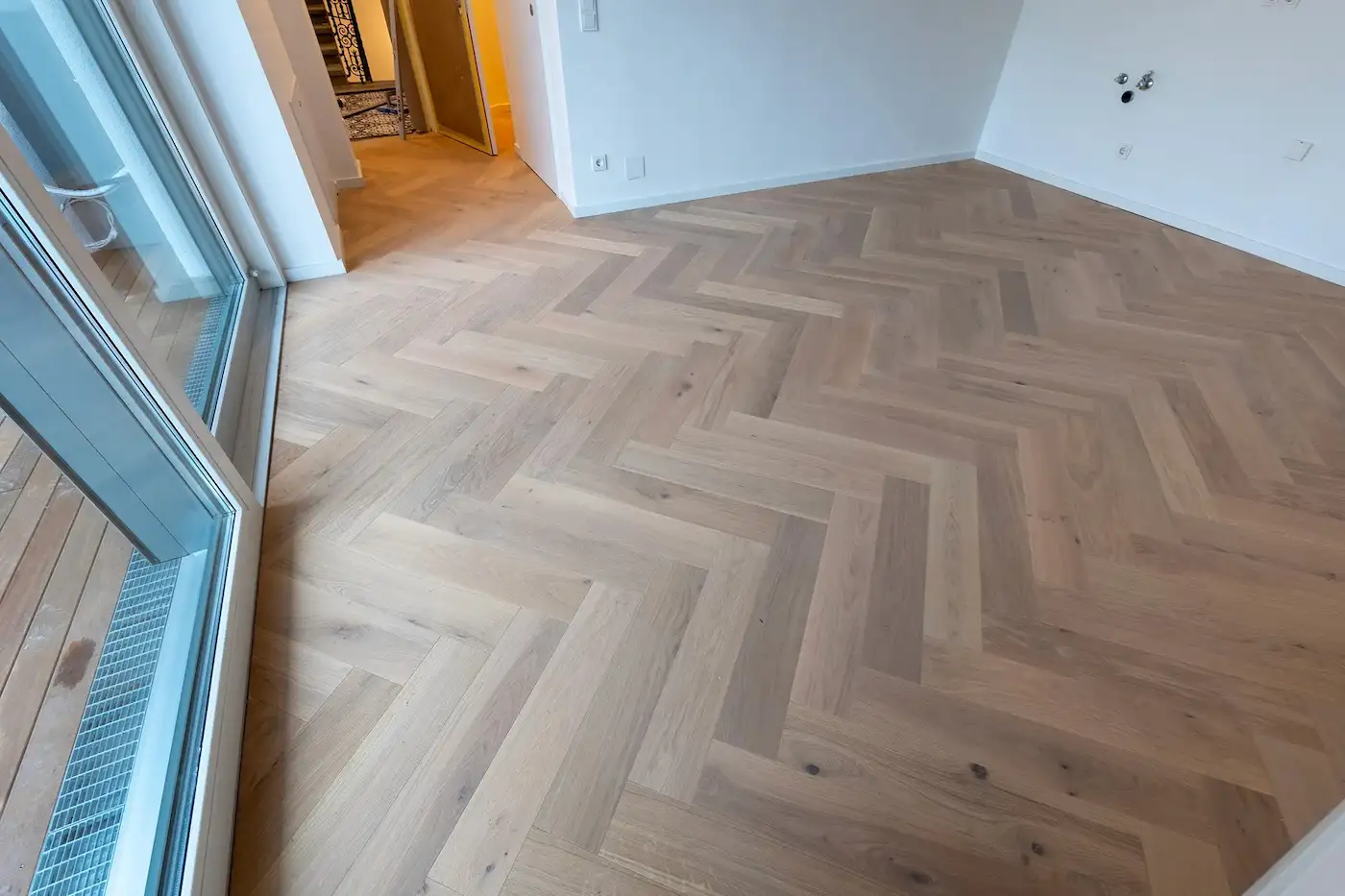 Großer Wohnraum mit bodentiefen Fenstern und neu verlegtem Fischgrät-Parkettboden