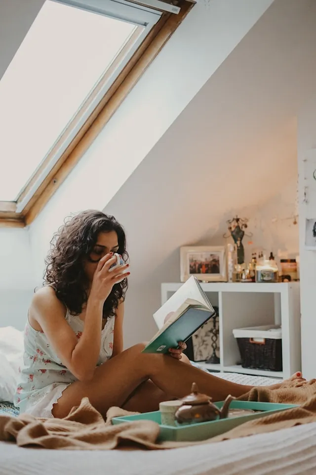 Woman with curly hair drinking coffee while looking at a laptop in a cozy home workspace.