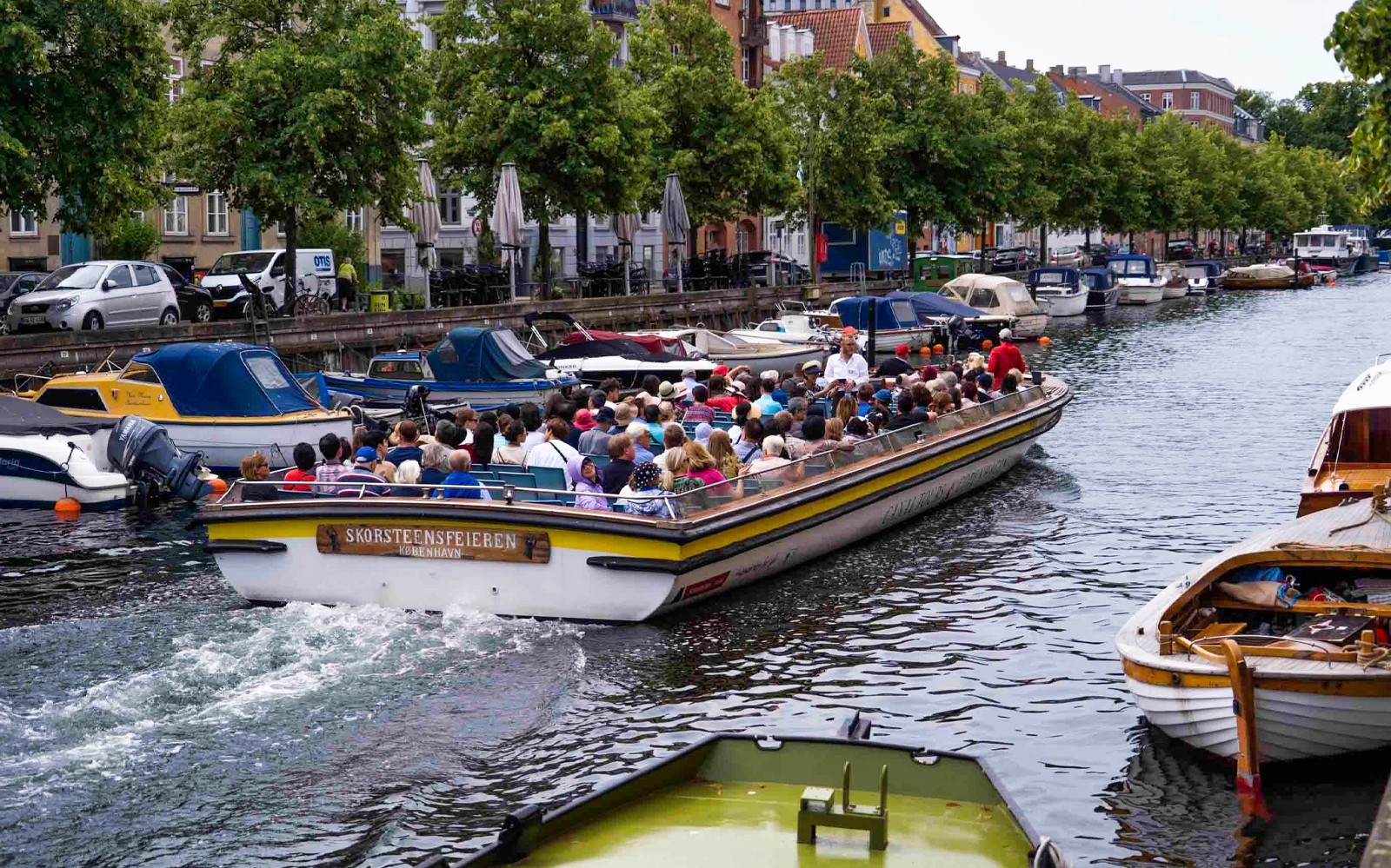 Hajókirándulás a koppenhágai csatornán turistákkal, színes épületek és kikötött hajók mellett elhaladva.
