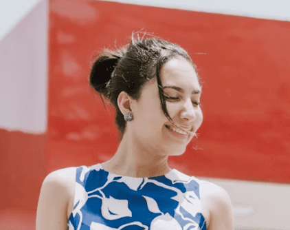 Jeune femme brune avec un chignon dehors devant un bâtiment orange et blanc