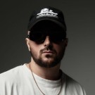 Portrait of a woman with long, smooth hair swept to the side, in a dark t-shirt, on a plain background.