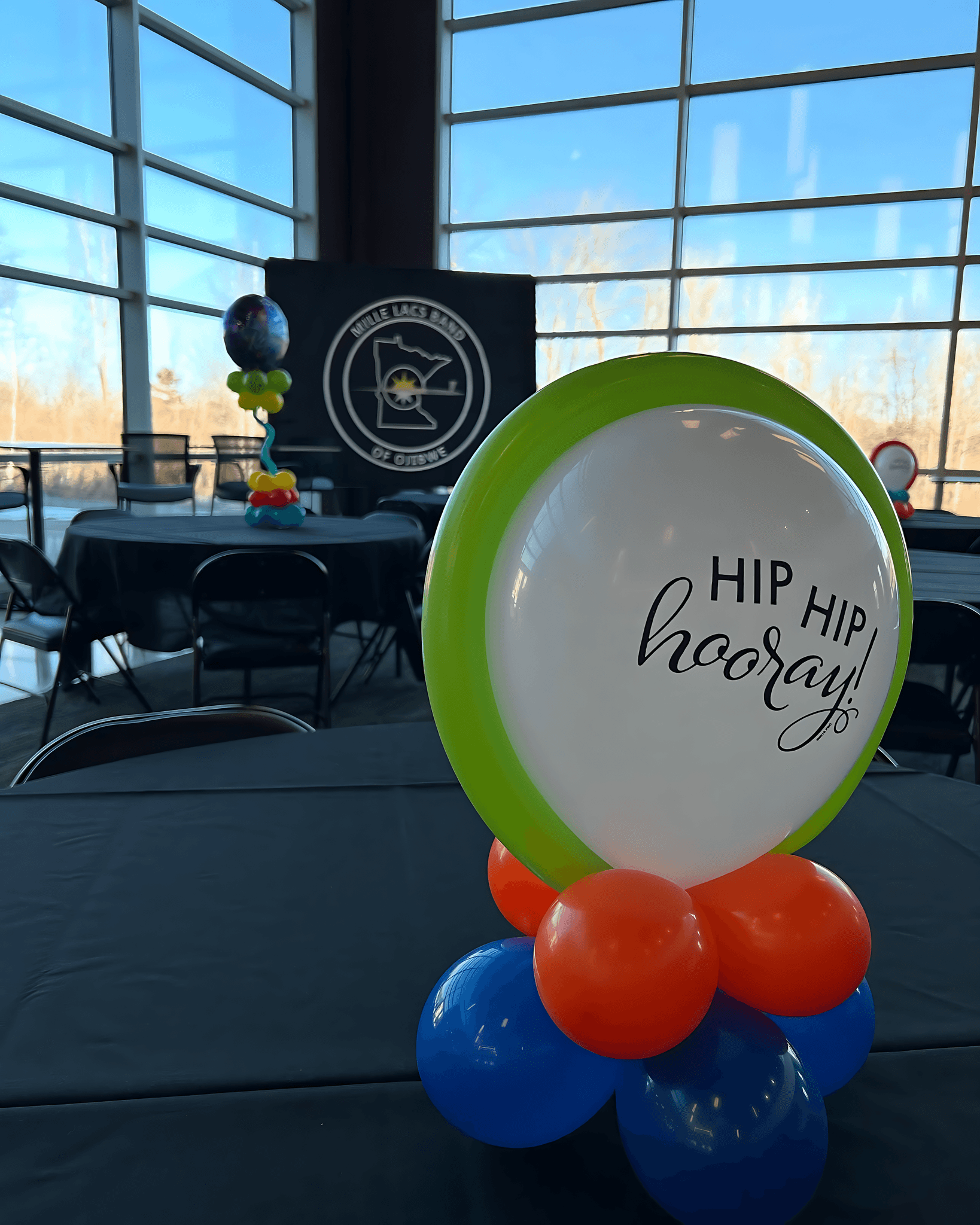 Balloon centerpiece with a large white balloon reading Let’s Party on a colorful blue, orange, and green base created by Be Bold Balloons