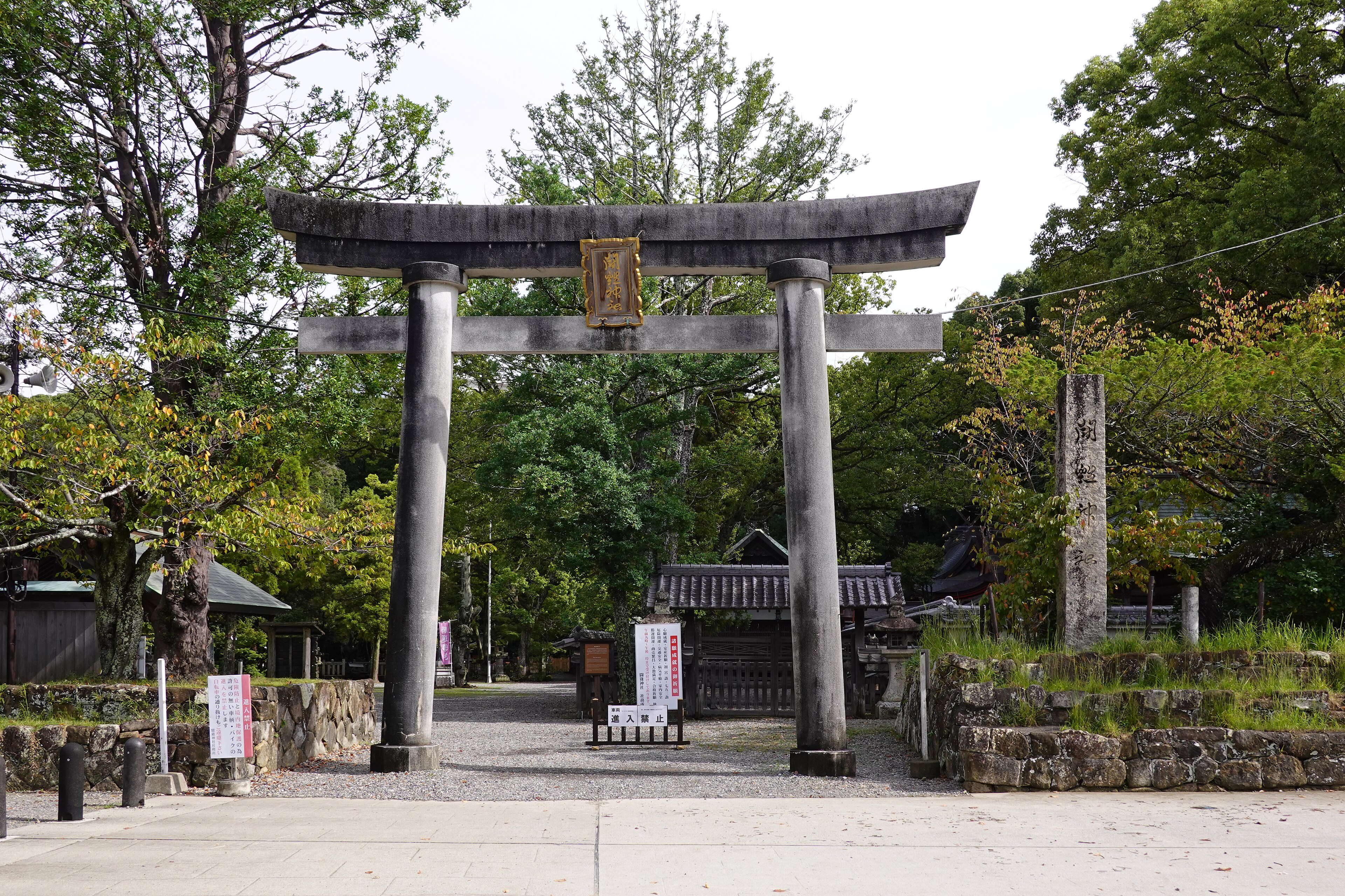 A stone torii marks the entrance to a wooded Shinto shrine in Japan.