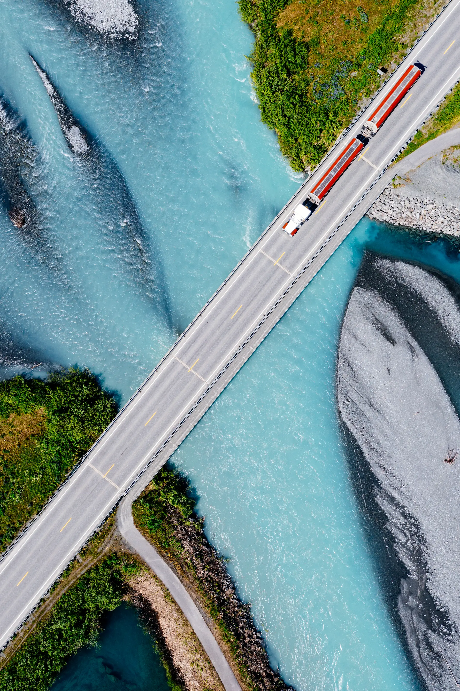 Aerial view of a semi-truck driving across a bridge over blue water representing truck insurance services