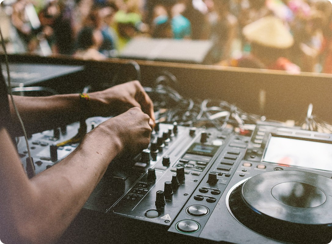Un DJ ajuste les boutons et commandes de sa table de mixage, entouré par la foule en arrière-plan.
