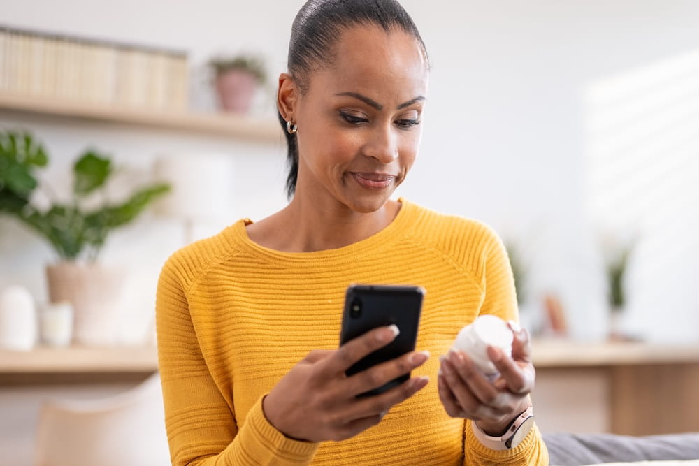 Woman looking at her phone while holding a medication bottle