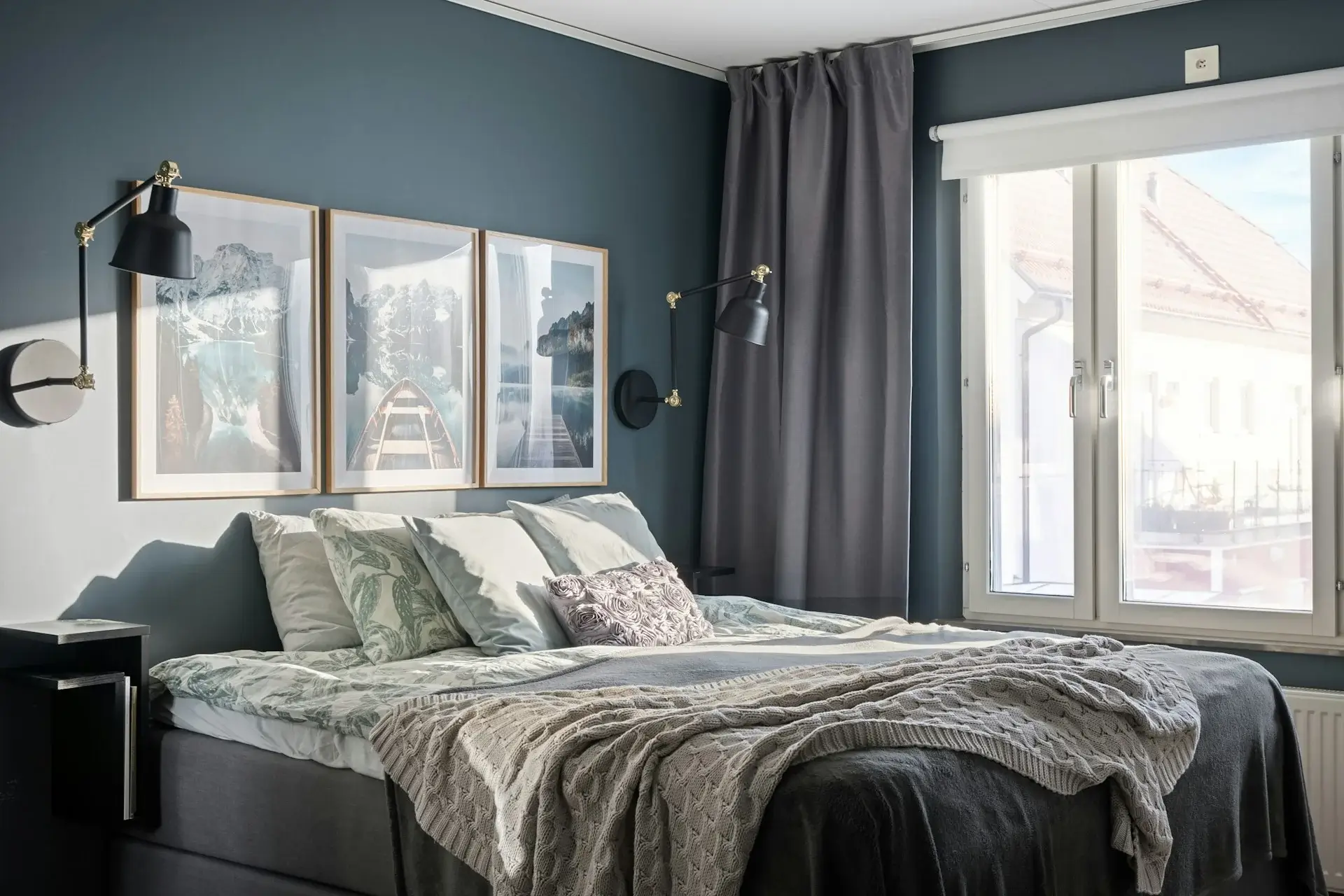 Cozy bedroom with blue accent wall, framed art, soft bedding, and window light.