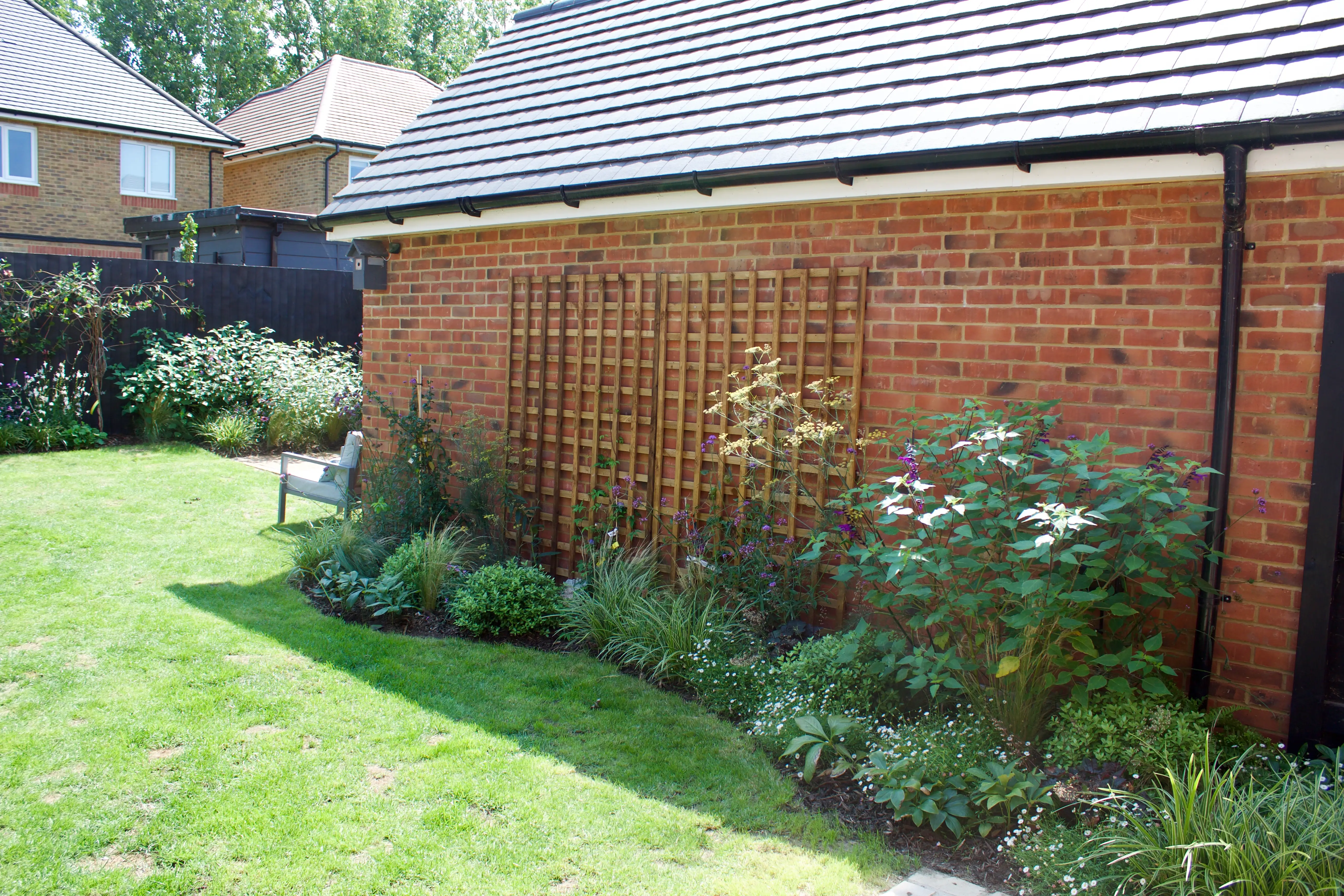A side view of a brick house with a well-maintained lawn and flower beds alongside the wall.