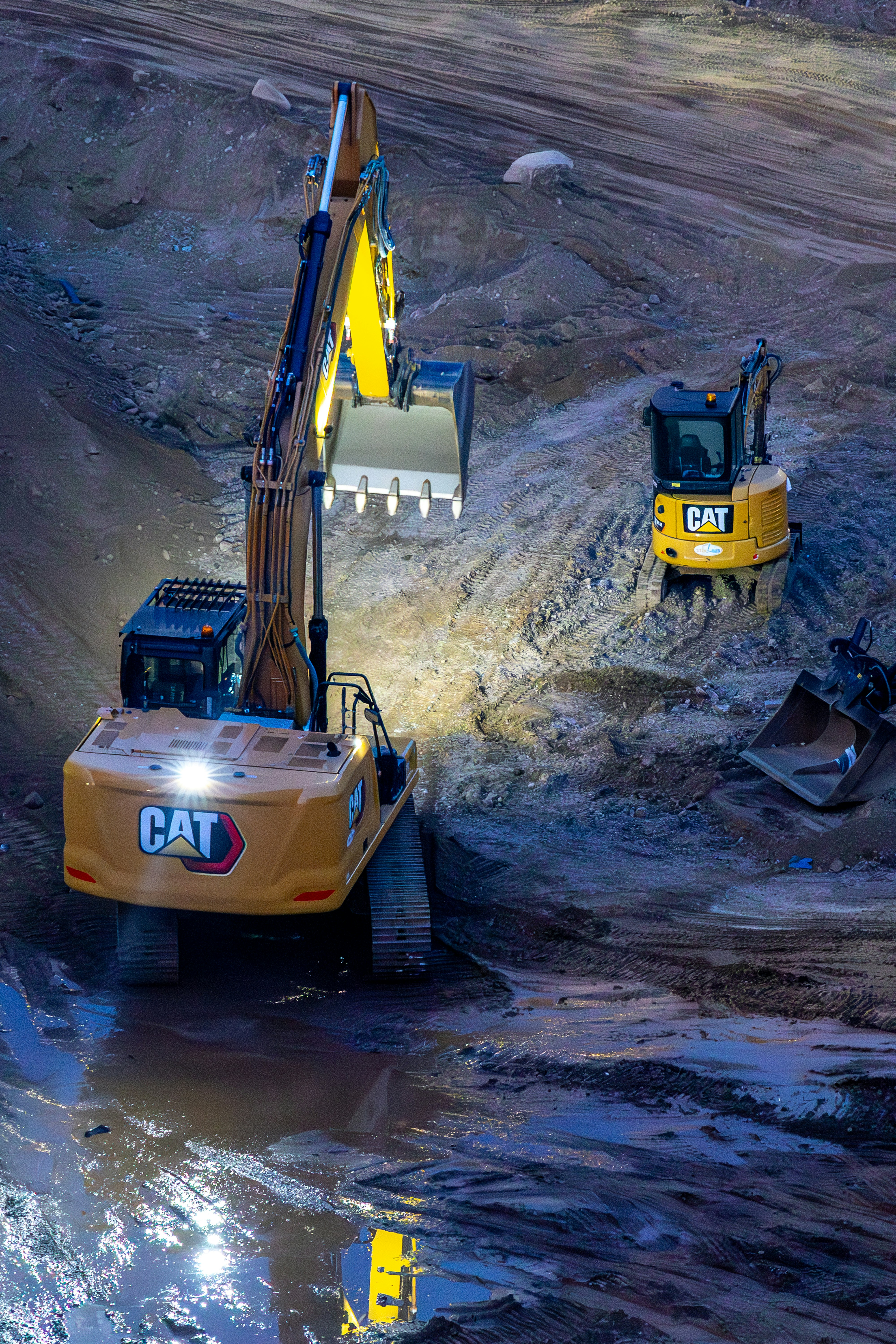 CAT excavators working at dusk on a wet, muddy earthworks site