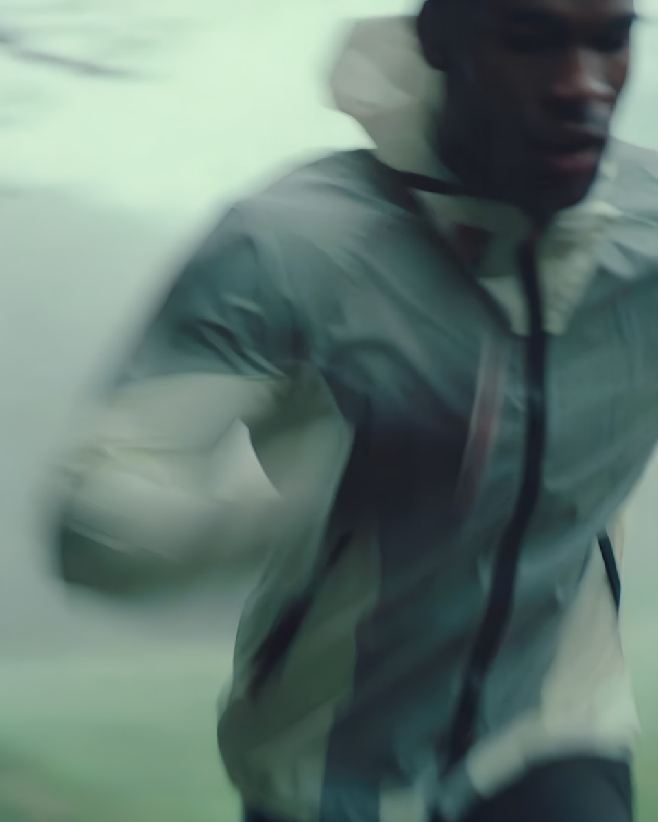 A person is running briskly, wearing a light-colored jacket, with a blurred background suggesting motion.