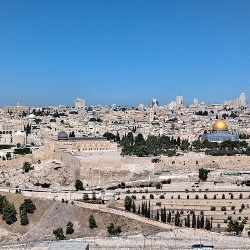 A view of Jerusalem's skyline featuring the Dome of the Rock, historic buildings, and modern cityscape under a clear blue sky.
