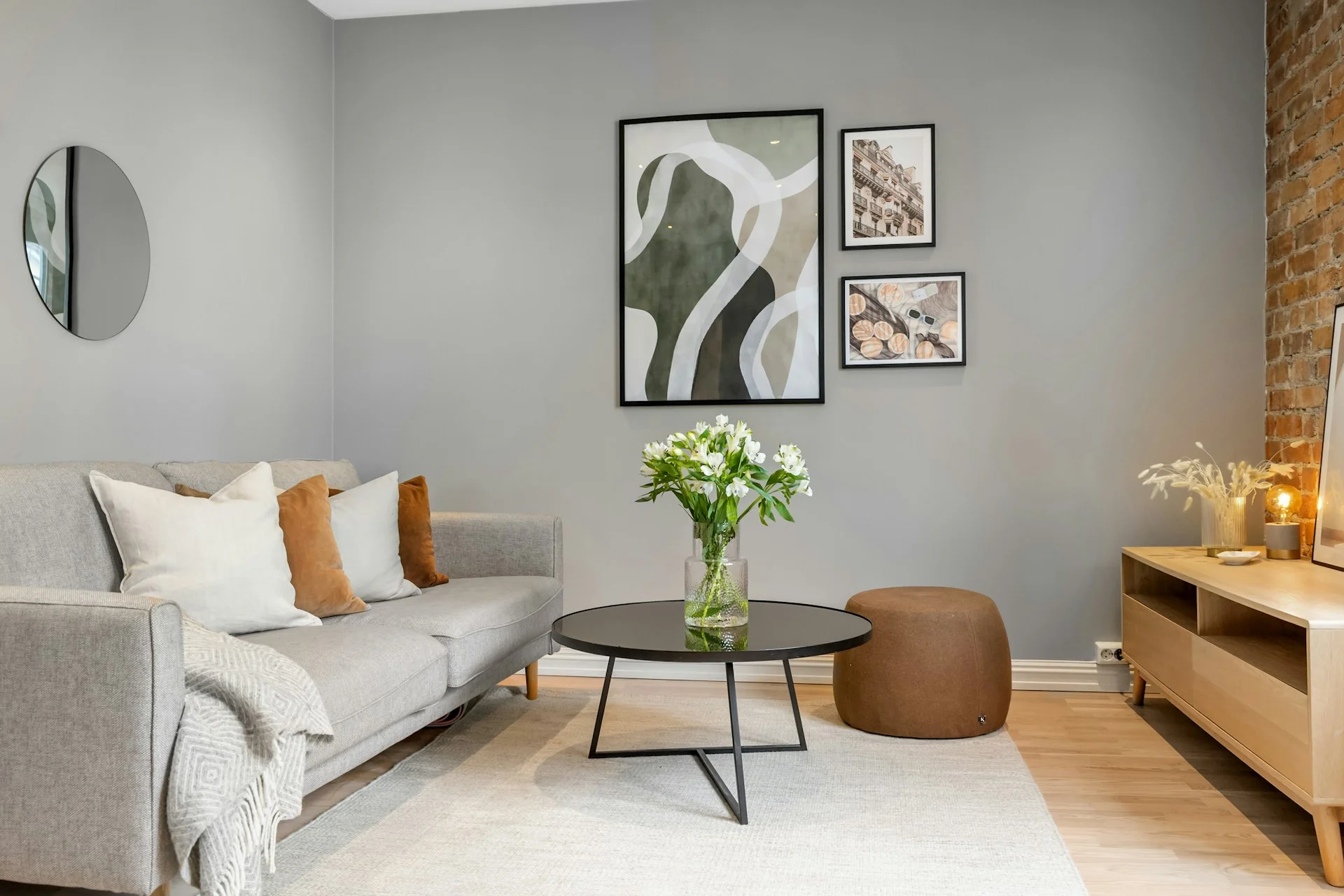 Modern living room with a grey sofa, neutral decor, framed wall art, and a round coffee table on a light rug.