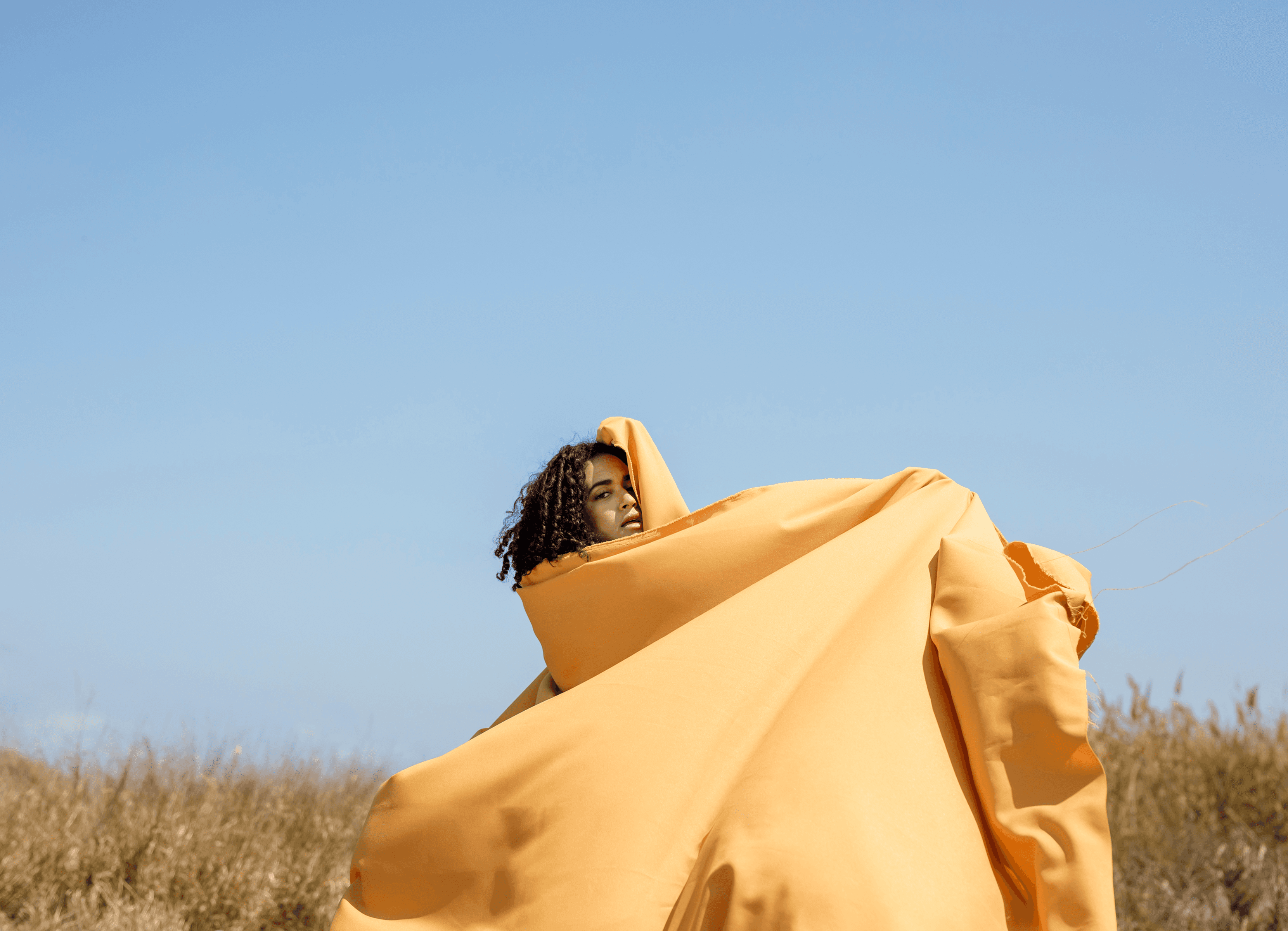 Creative portrait of a woman in yellow flowing fabric outdoors.