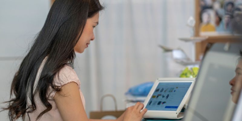 Seorang peniaga retail wanita sedang menggunakan sistem POS untuk menyemak inventori bisnes beliau.