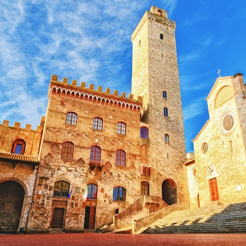 在蓝天下，拥有拱形窗户和高塔的历史石建筑；宽阔的台阶通向教堂入口。