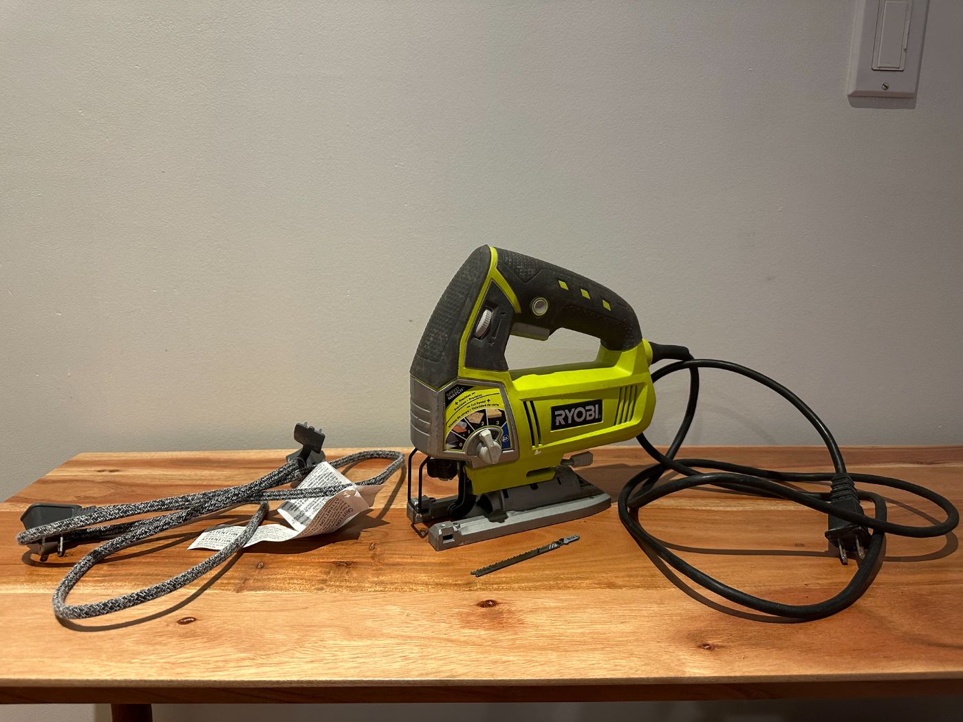 Scie sauteuse filaire Ryobi avec lame de rechange, posée sur une table en bois