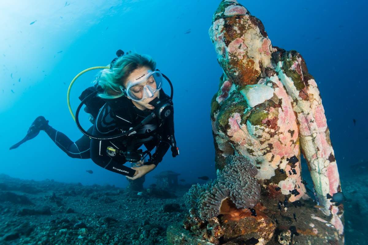 Diver next to a coral-covered underwater statue on an artificial reef near Amed, Bali