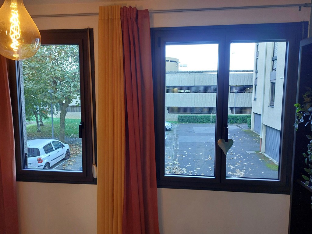 Fenêtre noire intérieure avec rideau orange et vue extérieure.