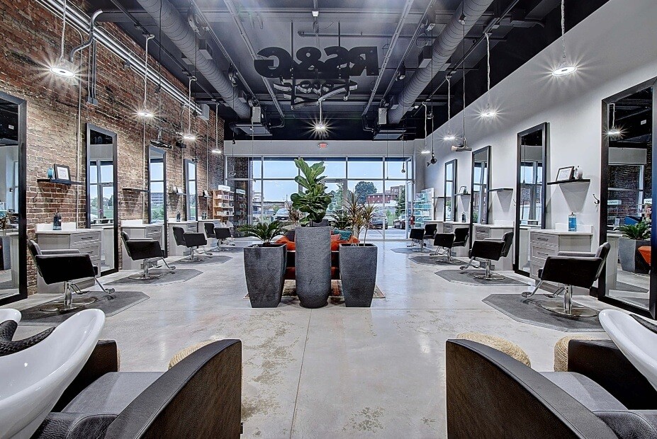 Interior of a modern salon with multiple styling stations, large mirrors, and a central seating area.
