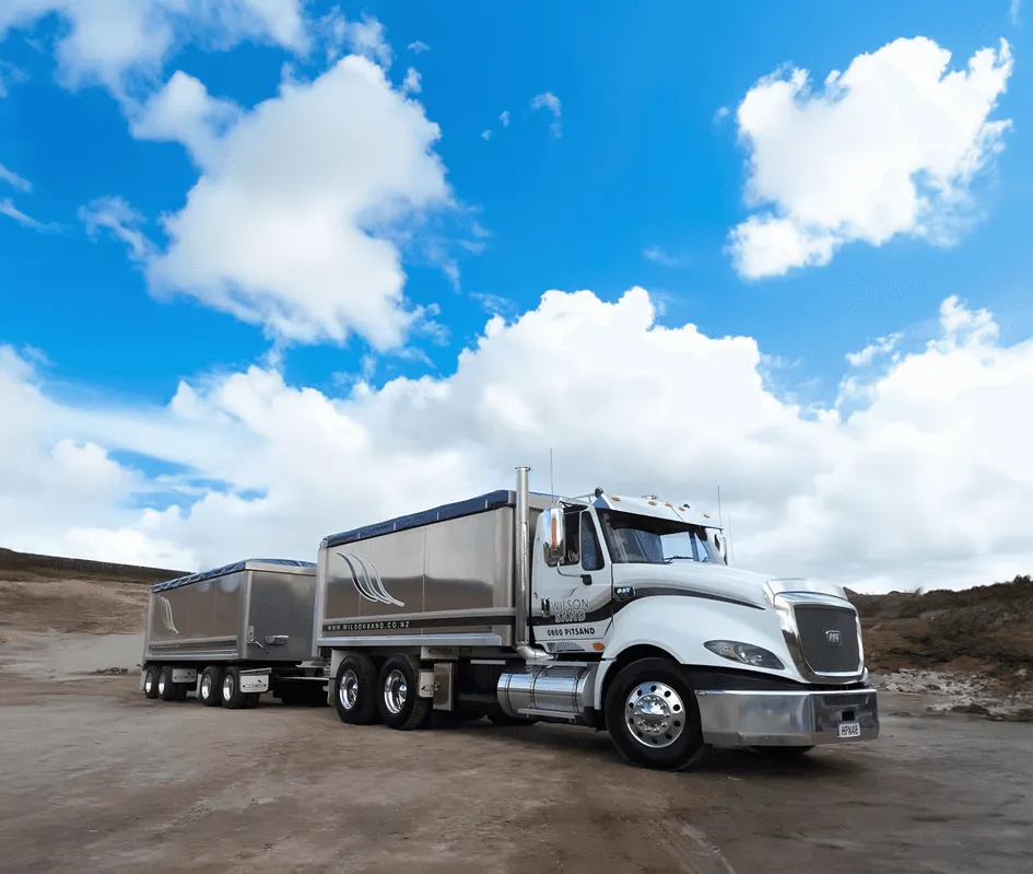 A large semi-truck and trailer parked in a sand quarry