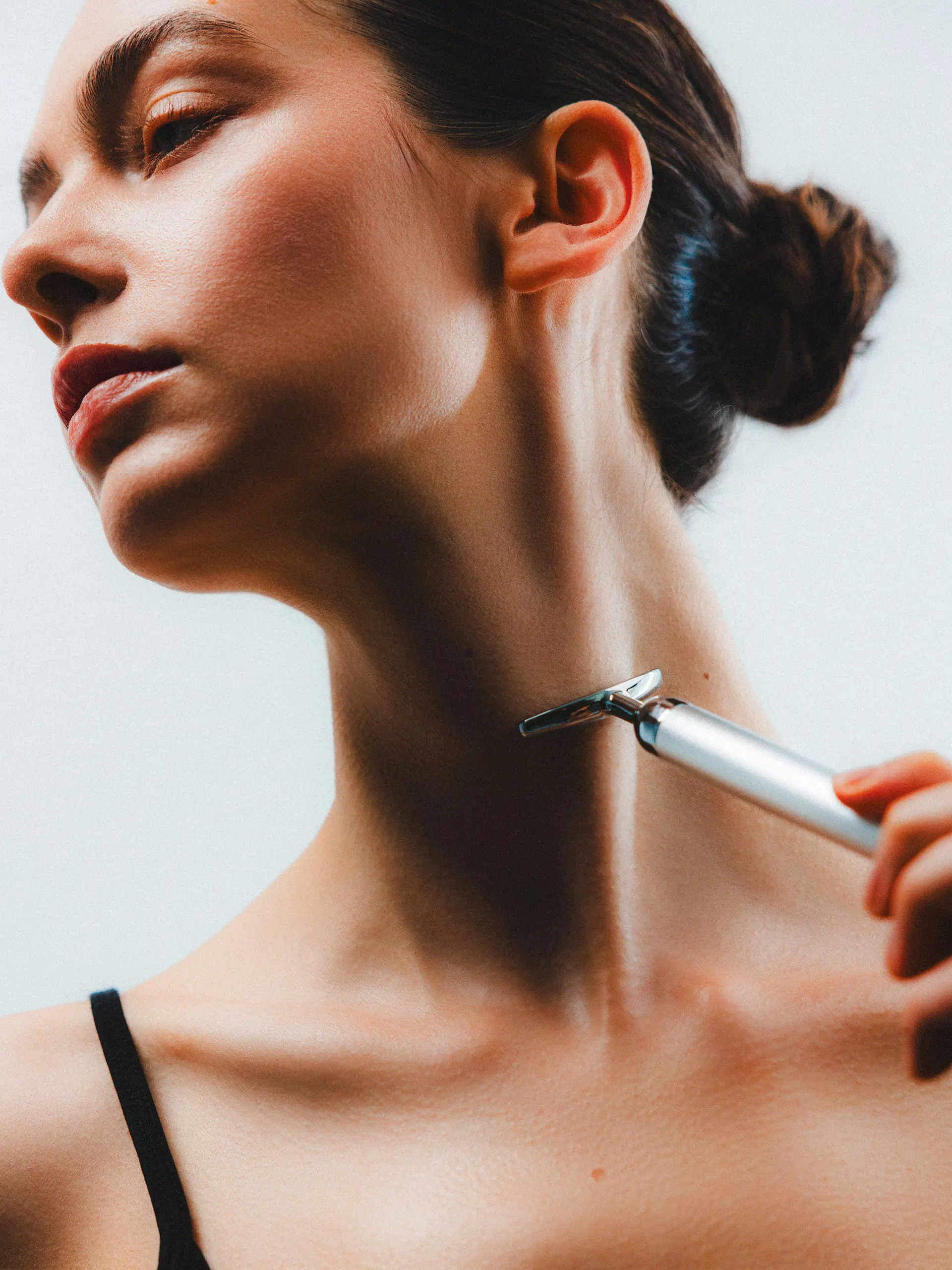 Woman using a facial razor on her neck for smooth skin care.