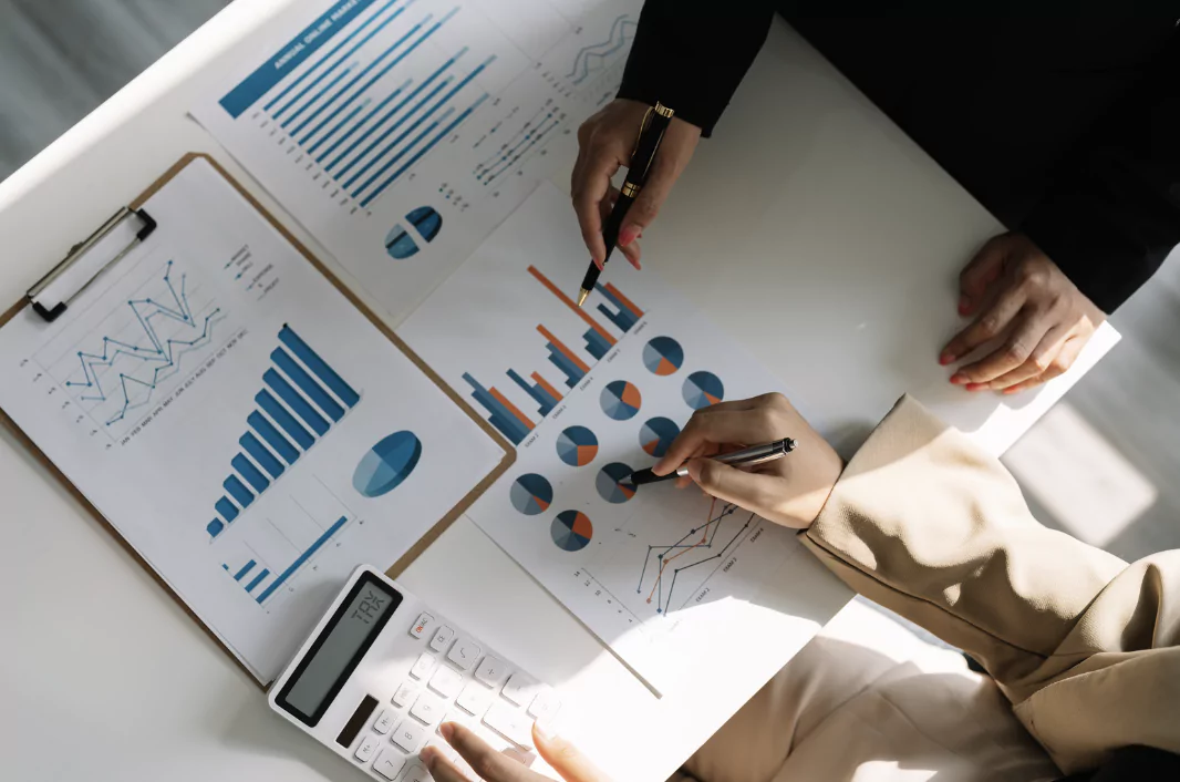 hands with pens going over pie charts and ar graphs at a desk