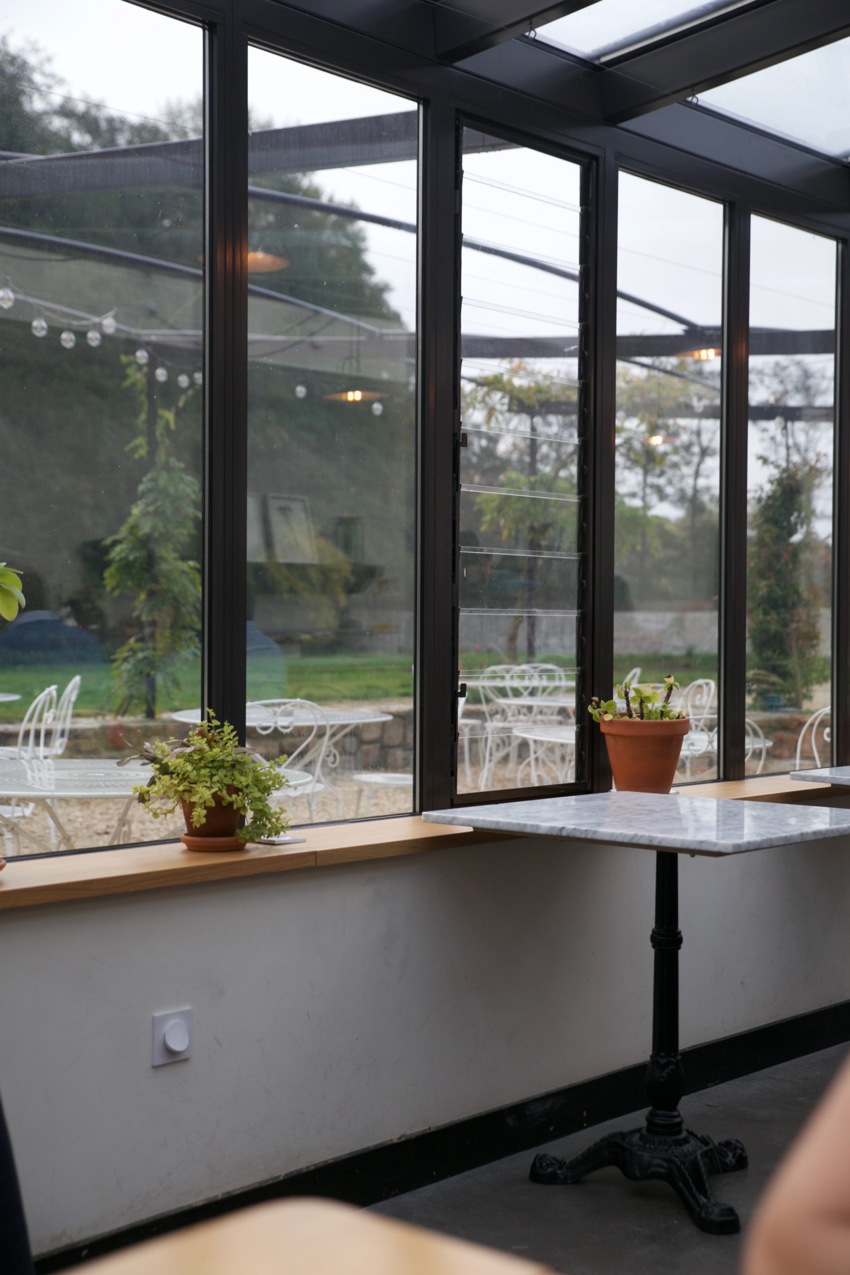 View through open glass doors of a conservatory looking out to a gravel terrace with white outdoor furniture
