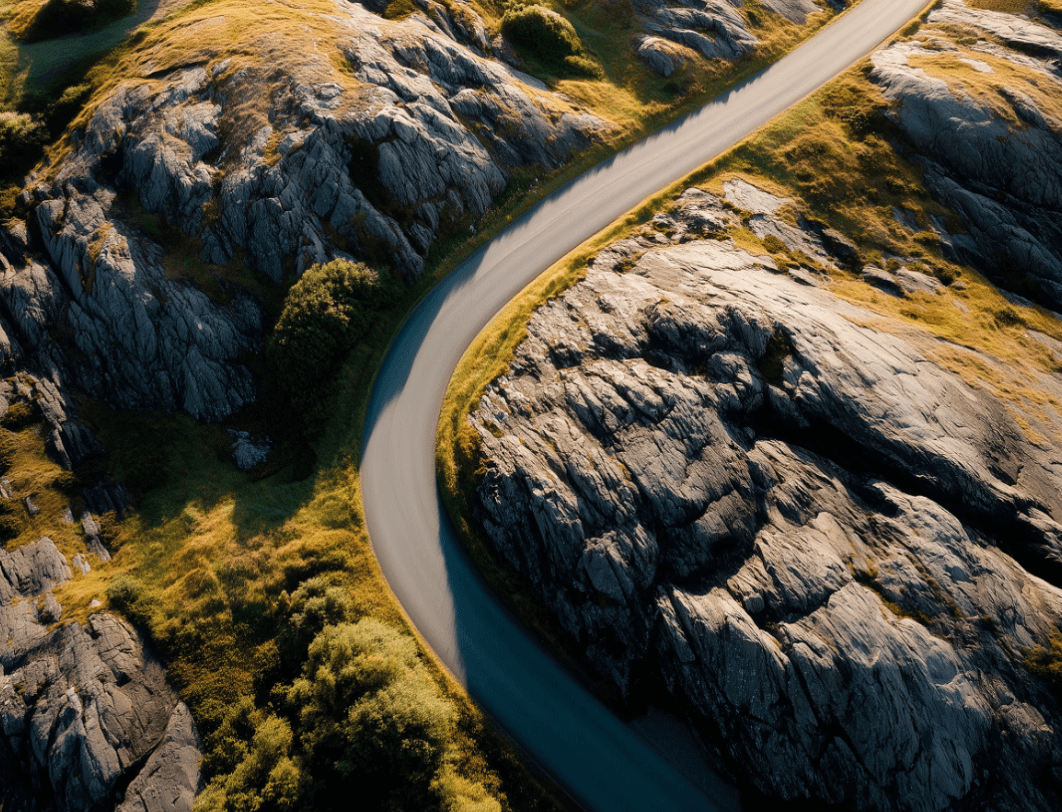 A young person with curly hair smiles at the camera while sitting in front of a laptop against a dark background.