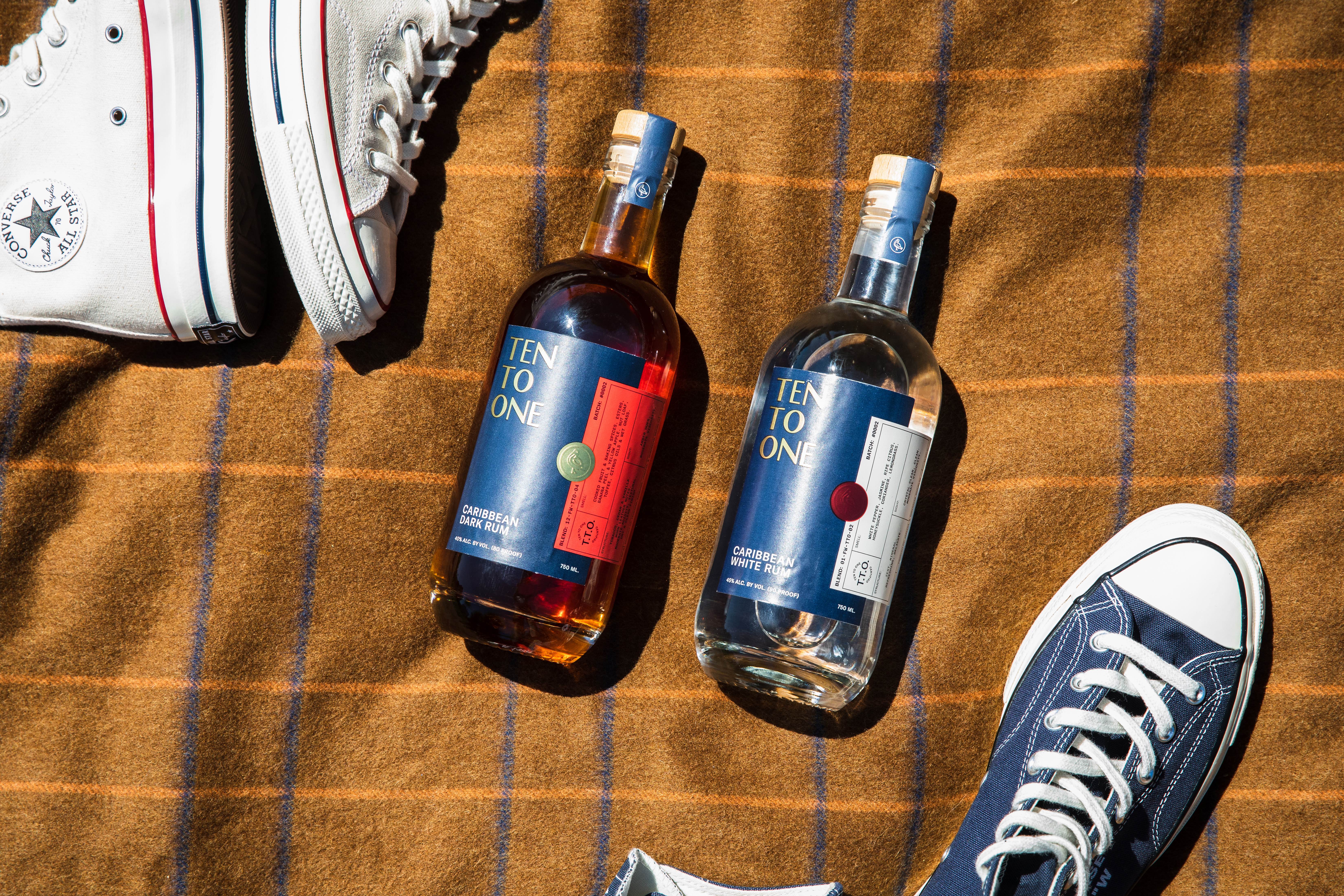 Two Ten To One rum bottles photographed top-down on a plaid blanket with Converse sneakers nearby.