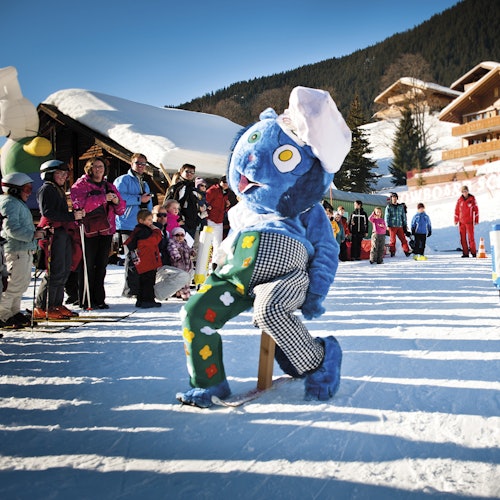 在一个山区滑雪度假村里，一个穿着蓝色生物服装的人在雪地上行走，周围有游客在观看。