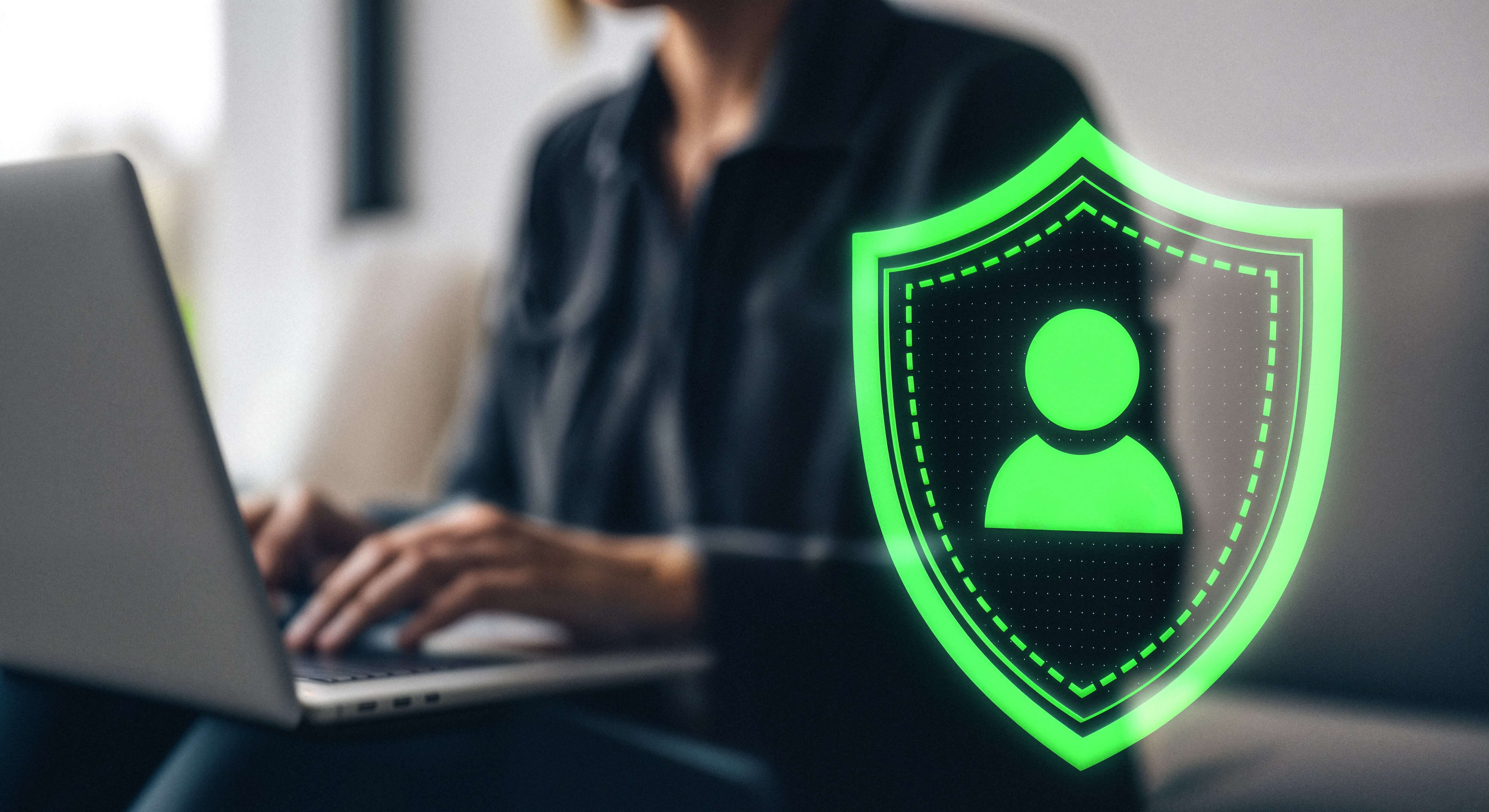 Overhead-style composite of a person working on a laptop with a prominent digital green identity shield.