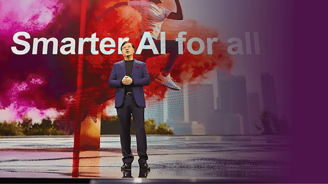 Keynote speaker in a blue blazer on stage in front of a large Smarter AI for all screen