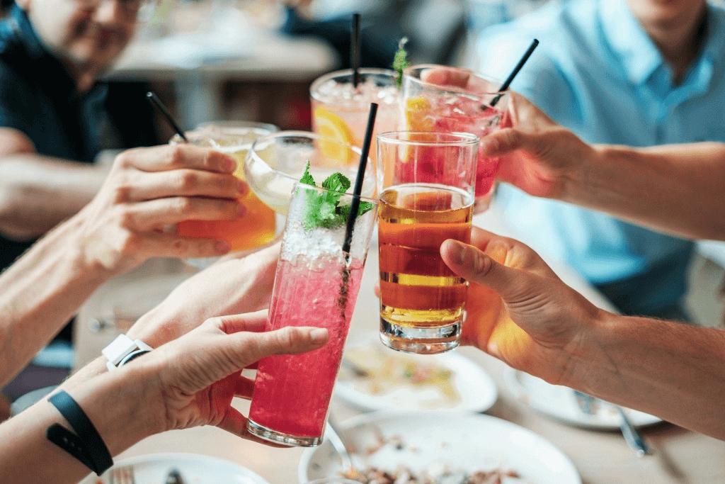 Group of people sitting at table, cheering their cocktails together