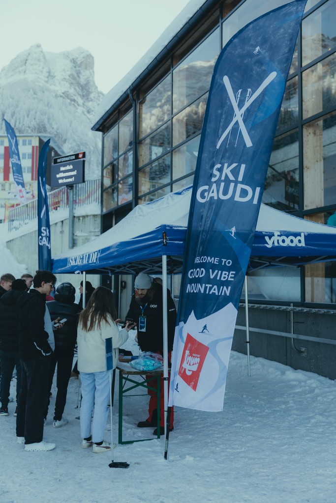 Ski Gaudi event registration booth on snowy mountain with visitors and promotional banners.