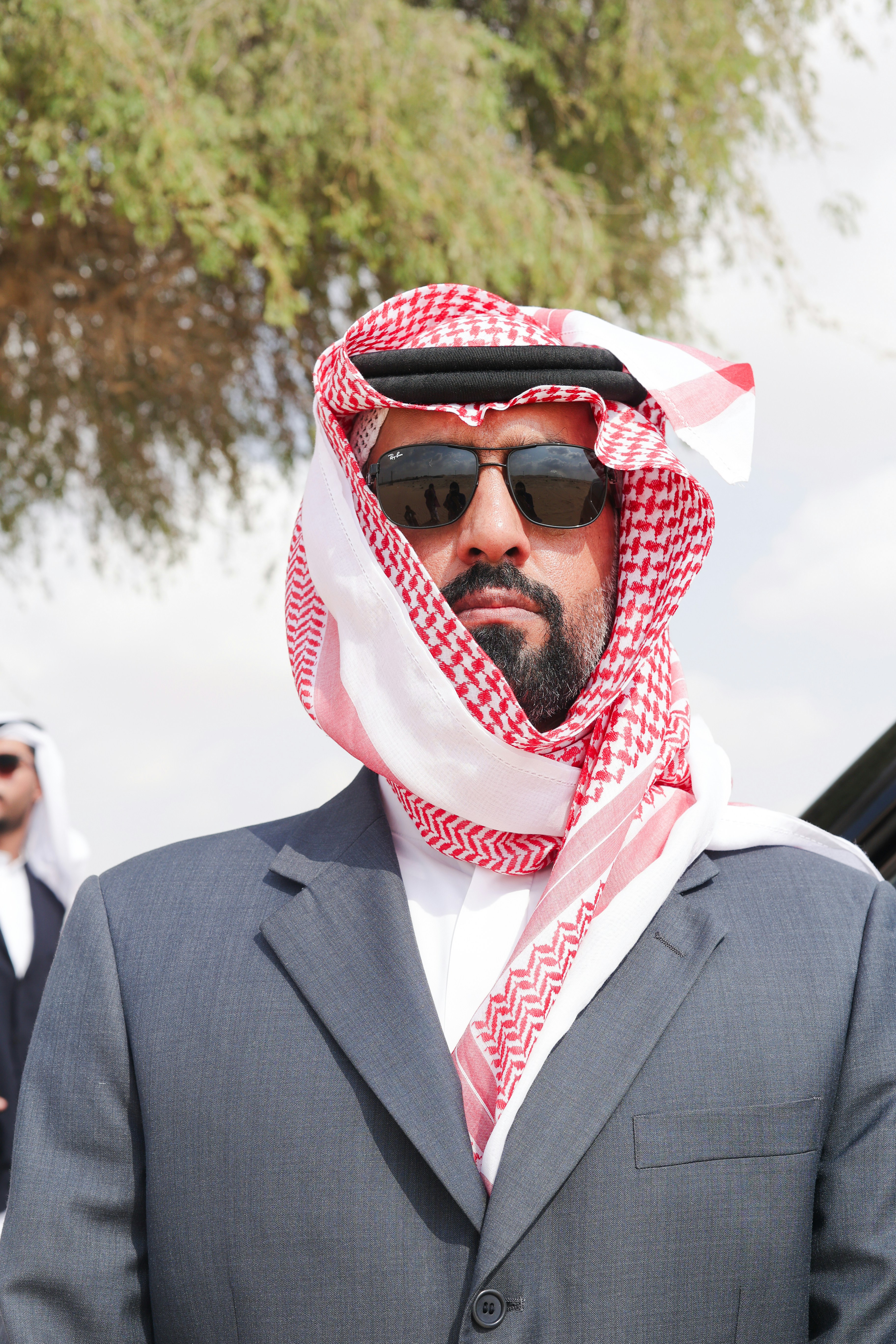 A man in a suit and sunglasses standing in front of a car