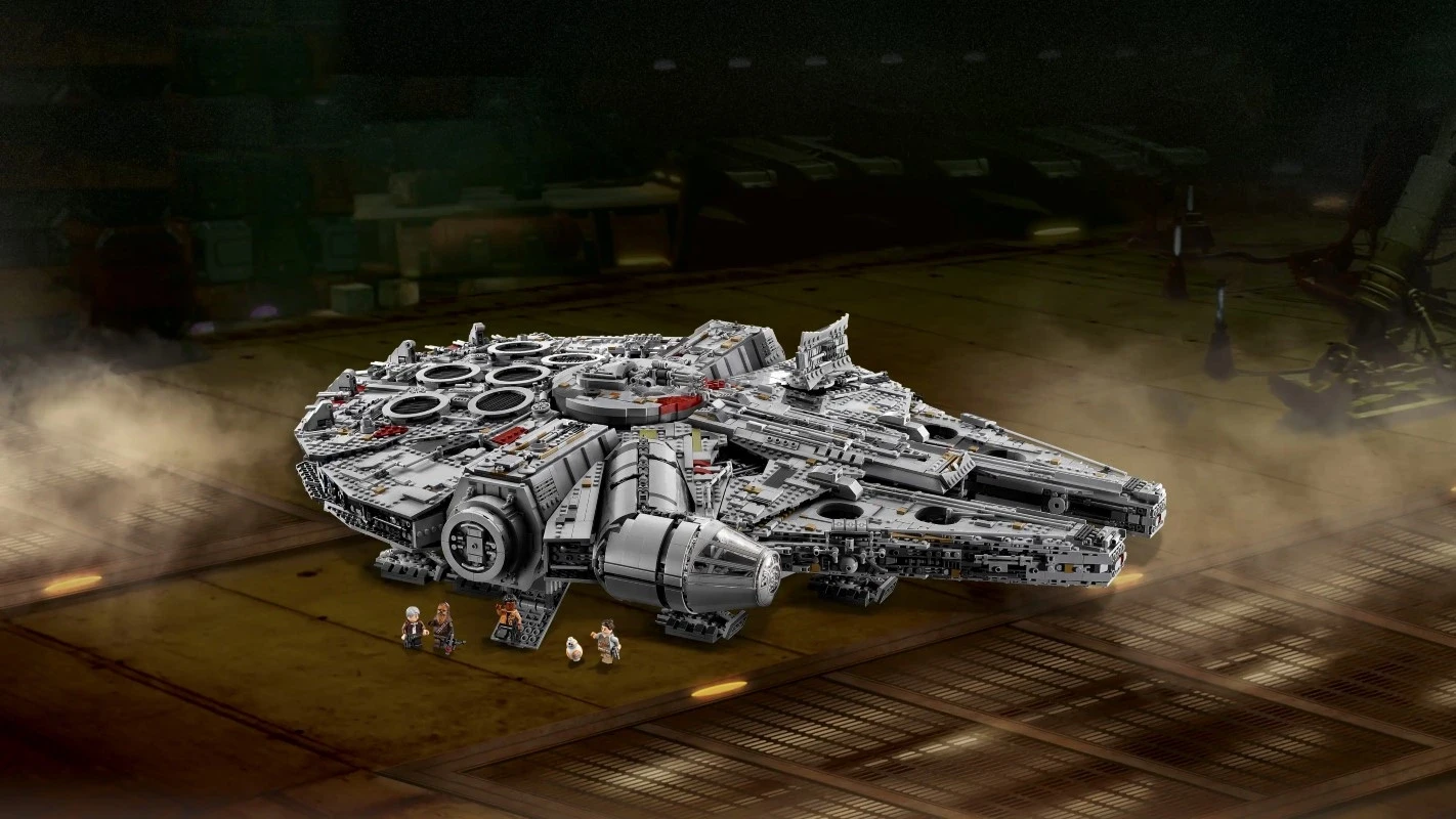 A highly detailed LEGO model of a spaceship resembling the iconic Millennium Falcon is displayed on a wooden surface, surrounded by several small figurines, with a backdrop of industrial-style dim lighting.