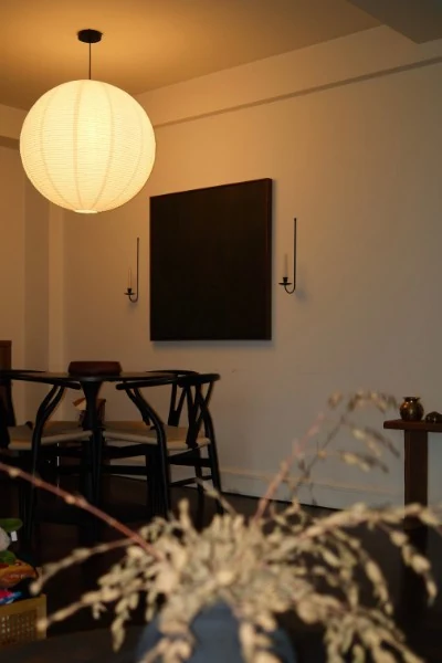 Dining room with a paper lantern pendant, black wishbone chairs, and a dark canvas between two candle sconces
