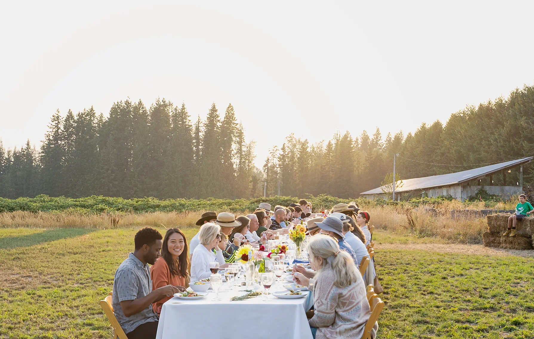 Residents and guests sharing a long outdoor meal together on farmland at Rooted Northwest.
