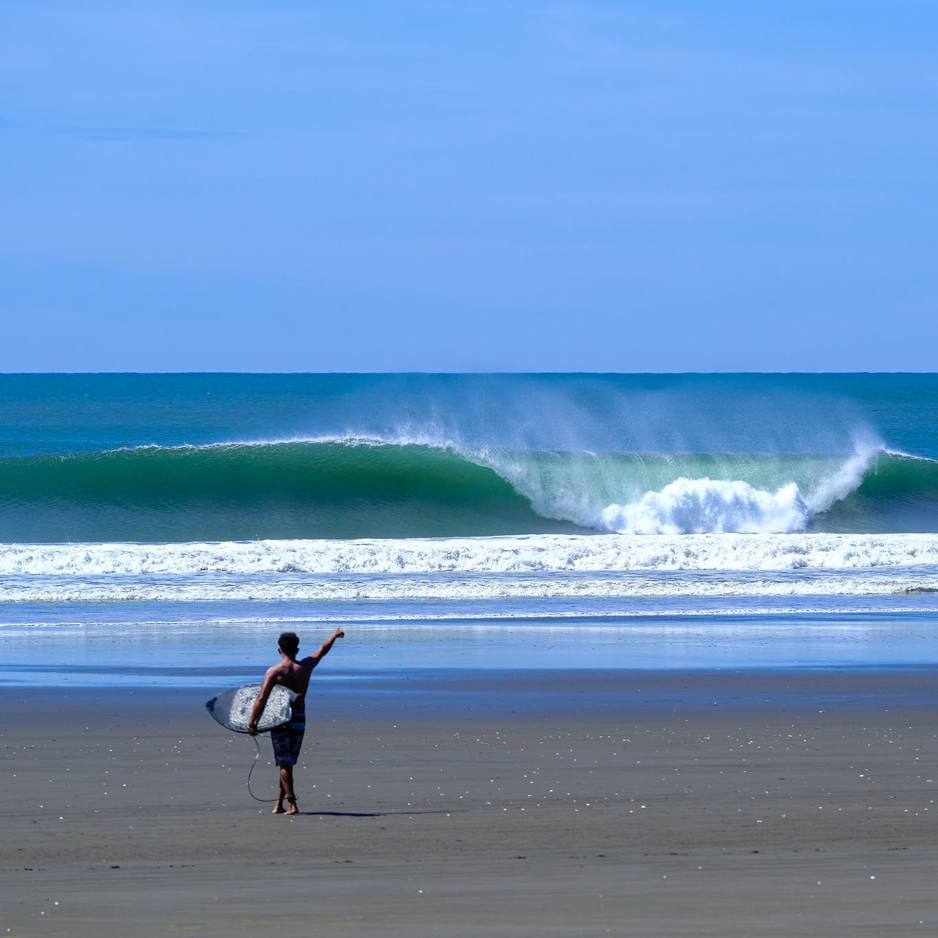 Man on beach with surfboard near large wave – surfboard rental in the-boom.