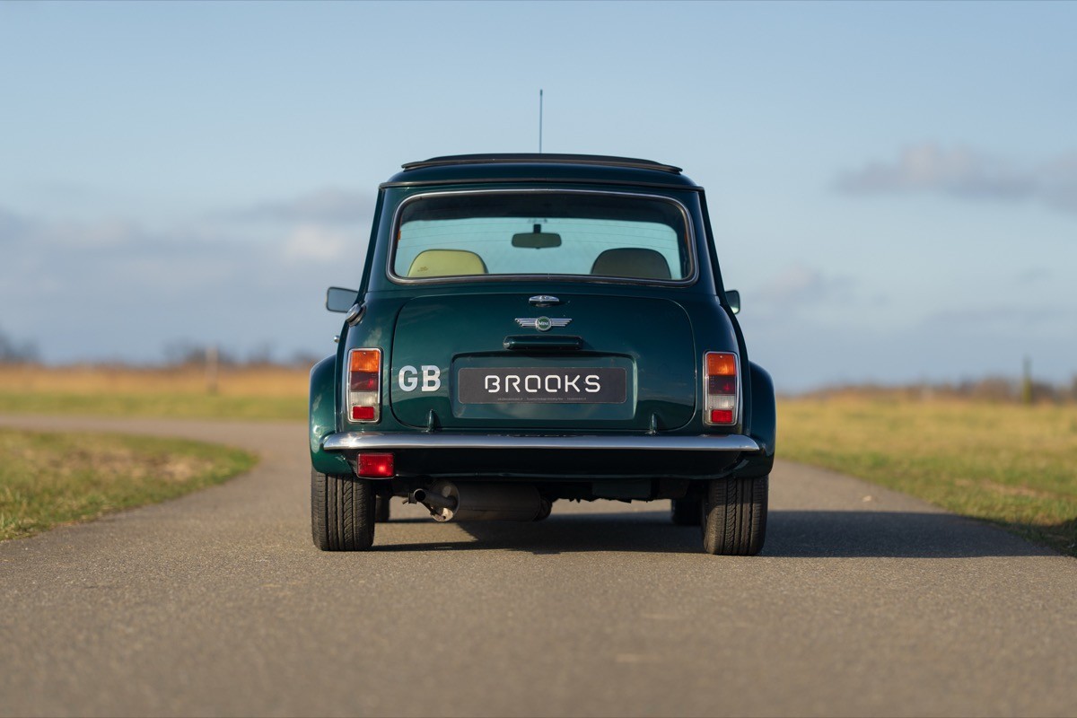 A classic green car parked on a road with an open landscape and blue sky in the background.